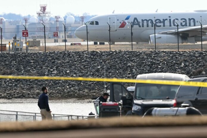 Un avión de American Airlines se prepara para despegar mientras los investigadores recogen restos de las aguas del río Potomac después de que el vuelo 5342 de American Airlines, al aproximarse al Aeropuerto Nacional Reagan, se estrellara en el río tras colisionar con un helicóptero del Ejército de Estados Unidos, cerca de Washington, este jueves. Crédito: Andrew Caballero-Reynolds/AFP/Getty Images.